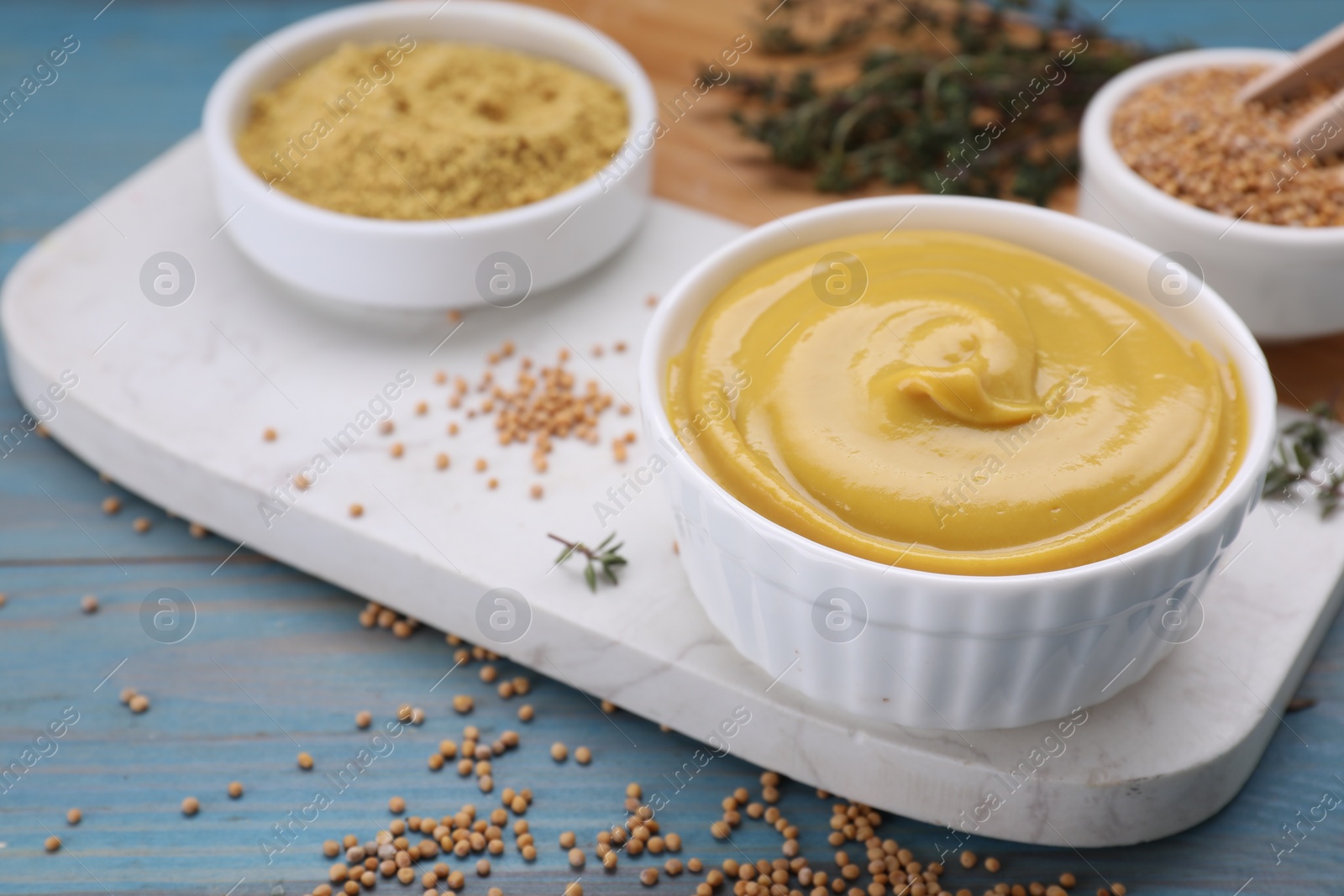 Photo of Delicious mustard and seeds on light blue wooden table, closeup