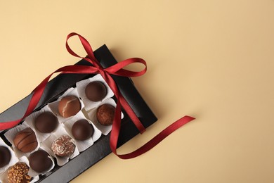 Box with delicious chocolate candies on beige table, top view. Space for text