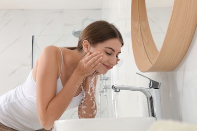 Photo of Young woman washing her face with water in bathroom