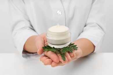 Female dermatologist holding jar of skin care product at table, closeup