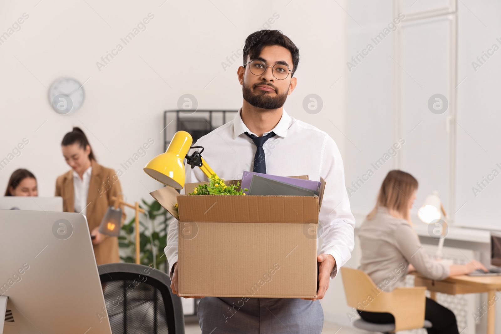 Photo of Unemployment problem. Frustrated man with box of personal belongings in office