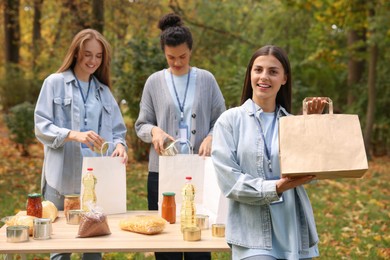 Photo of Group of volunteers packing food products at table in park. Woman with paper bag outdoors