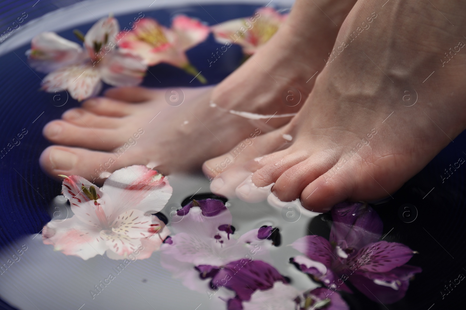 Photo of Woman soaking her feet in bowl with water and flowers, closeup. Spa treatment