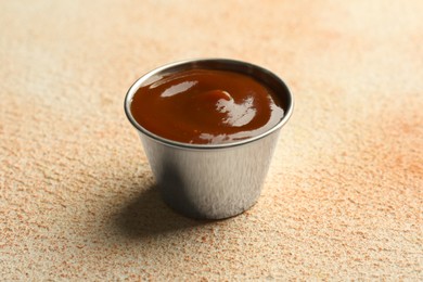 Tasty barbeque sauce in bowl on beige textured table, closeup