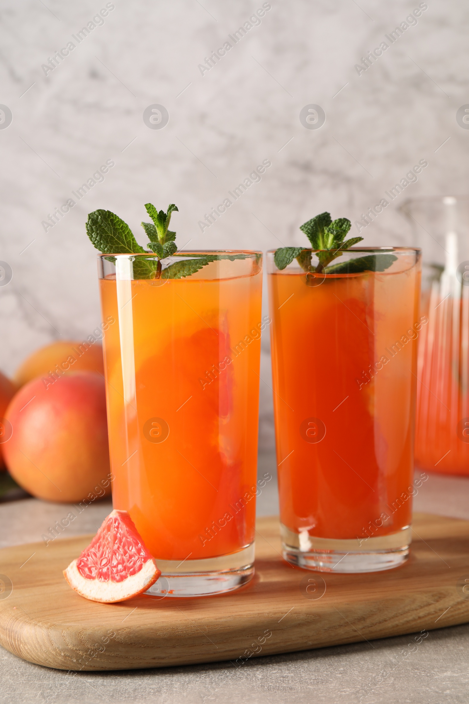 Photo of Tasty freshly made grapefruit juice, fruit and mint on light grey table