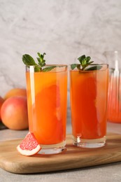 Photo of Tasty freshly made grapefruit juice, fruit and mint on light grey table