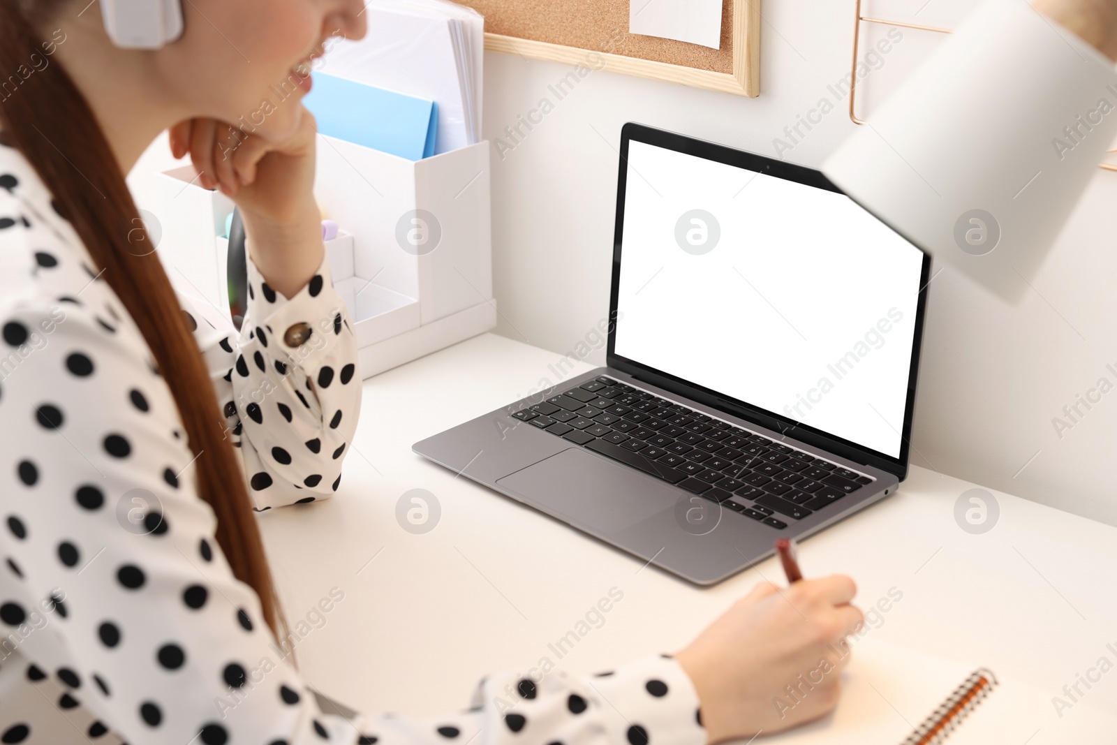 Photo of E-learning. Woman taking notes during online lesson at table indoors, closeup