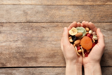 Photo of Woman holding different dried fruits and nuts on wooden background, top view. Space for text