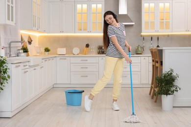Photo of Enjoying cleaning. Happy woman in headphones dancing with mop in kitchen