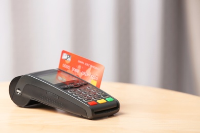 Modern payment terminal with credit card on table indoors. Space for text