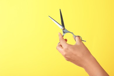 Hairdresser holding professional scissors and space for text on yellow background, closeup. Haircut tool
