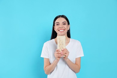 Happy young woman with delicious shawarma on light blue background