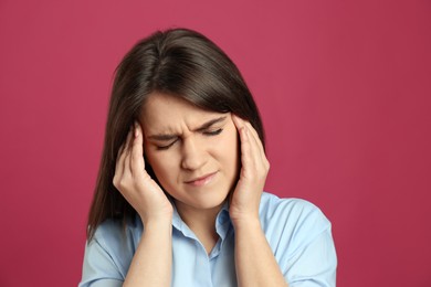 Young woman suffering from migraine on crimson background