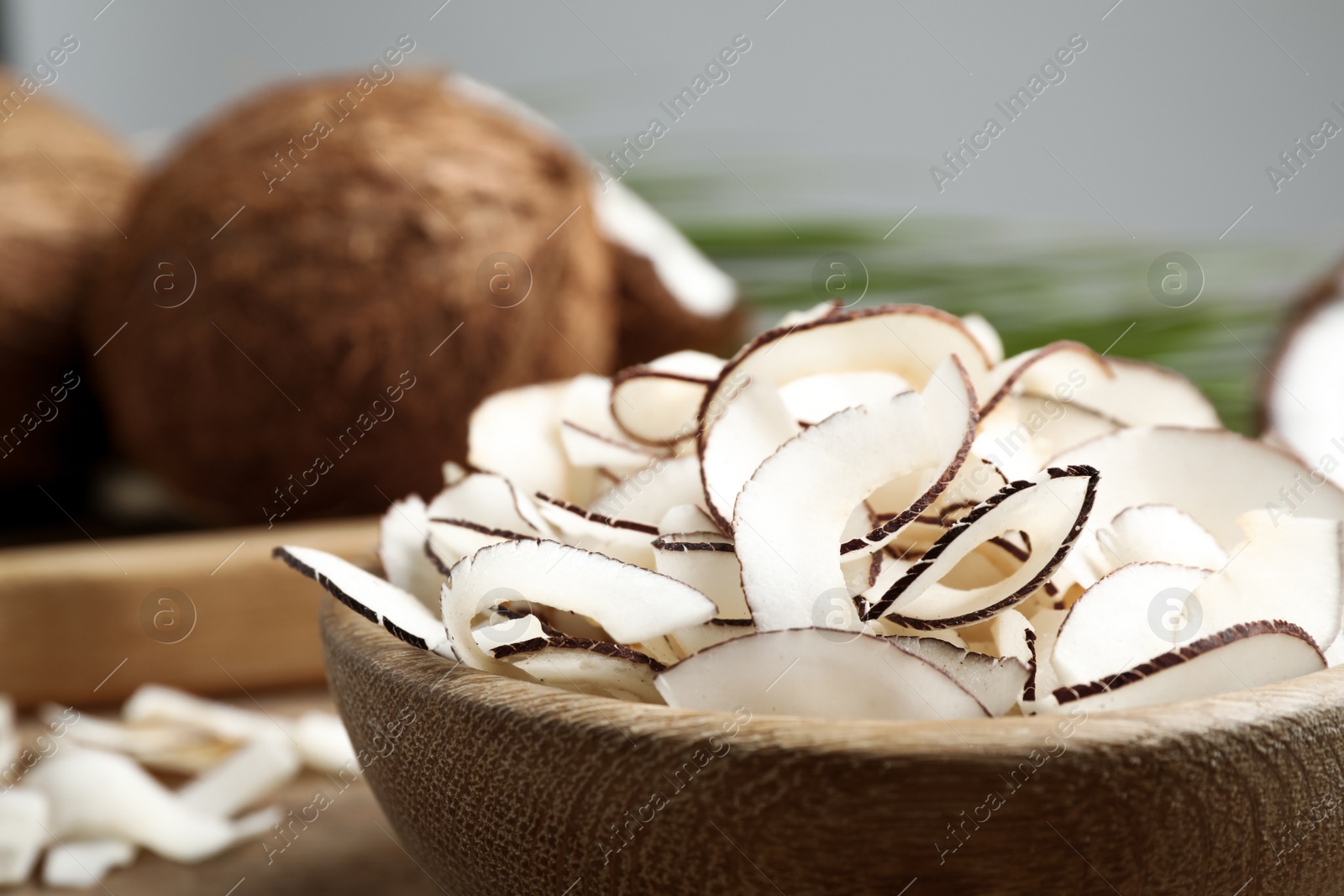 Photo of Tasty coconut chips in wooden bowl, closeup