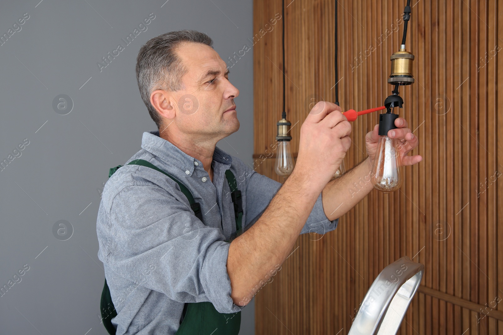 Photo of Electrician with screwdriver repairing ceiling lamp indoors