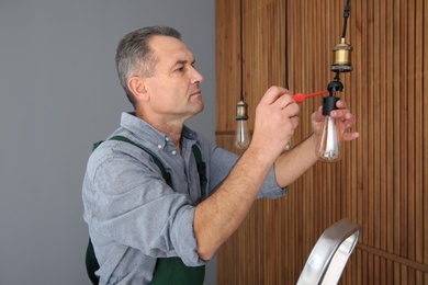 Photo of Electrician with screwdriver repairing ceiling lamp indoors