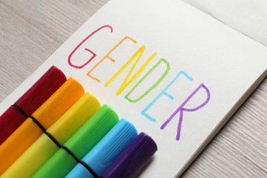 Photo of Notebook with word Gender and felt tip pens on wooden table, closeup
