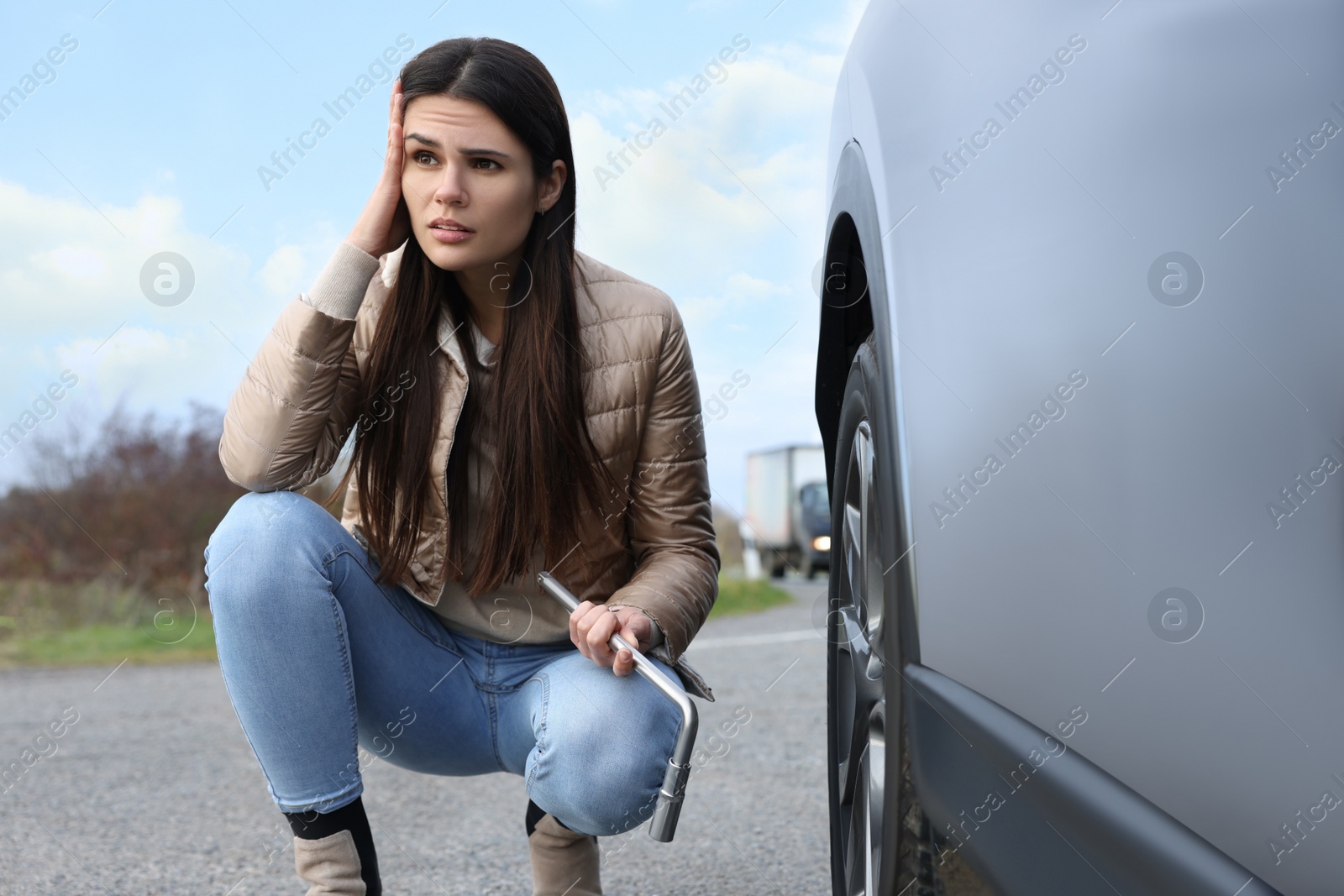 Photo of Worried young woman near car with punctured wheel on roadside