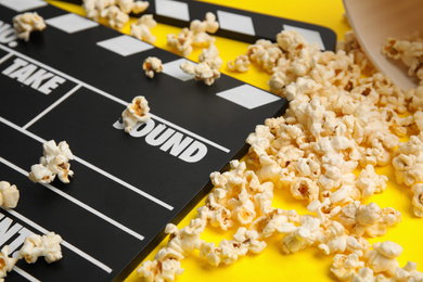 Tasty pop corn and clapboard on yellow background, closeup