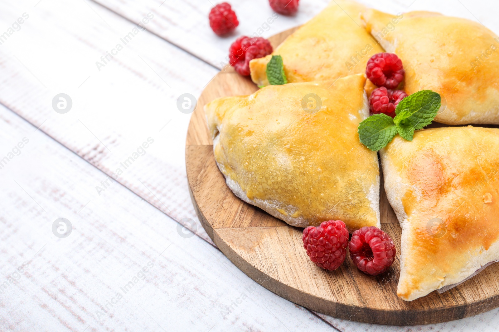 Photo of Delicious samosas with raspberries on white wooden table, closeup. Space for text