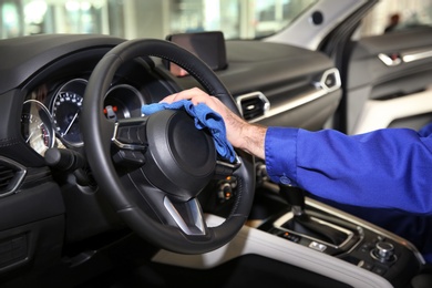 Worker cleaning automobile steering wheel with rag, closeup. Car wash service