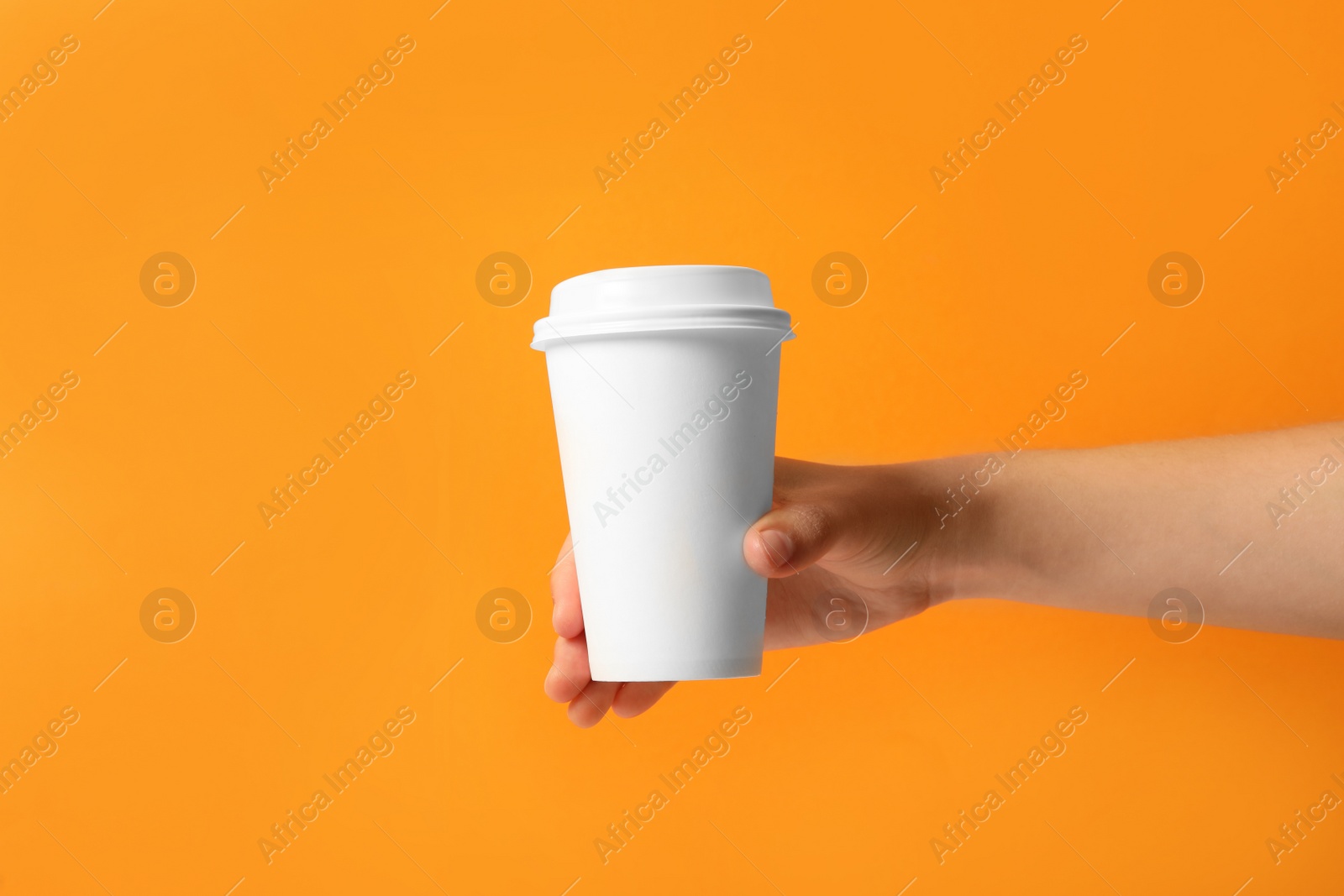 Photo of Woman holding takeaway paper coffee cup on orange background, closeup