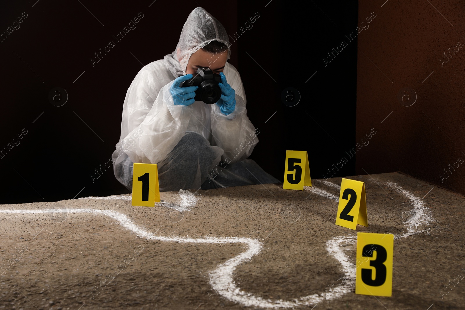 Photo of Criminologist in protective suit working at crime scene outdoors