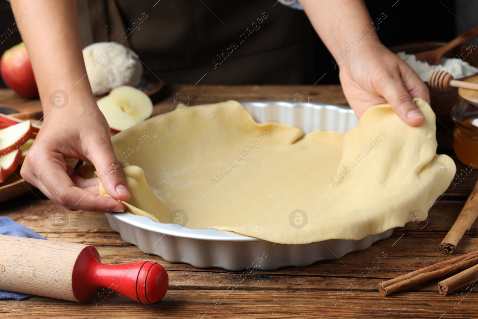 Photo of Woman putting dough for apple pie into baking dish at wooden table, closeup