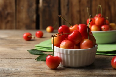 Sweet red cherries in bowl on wooden table, space for text