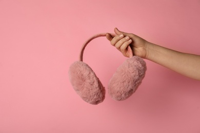 Photo of Woman holding stylish winter earmuffs on pink background, closeup