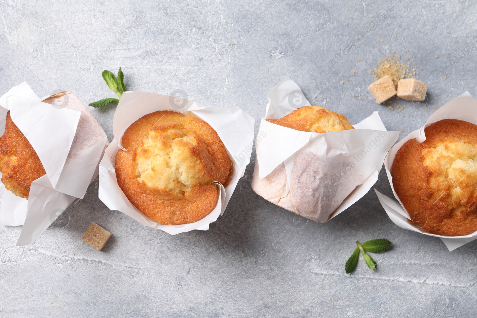 Photo of Delicious sweet muffins and brown sugar on light grey textured table, flat lay