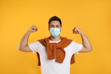 Man with protective mask showing muscles on yellow background. Strong immunity concept