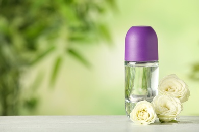 Photo of Deodorant container and roses on white wooden table against blurred background. Space for text