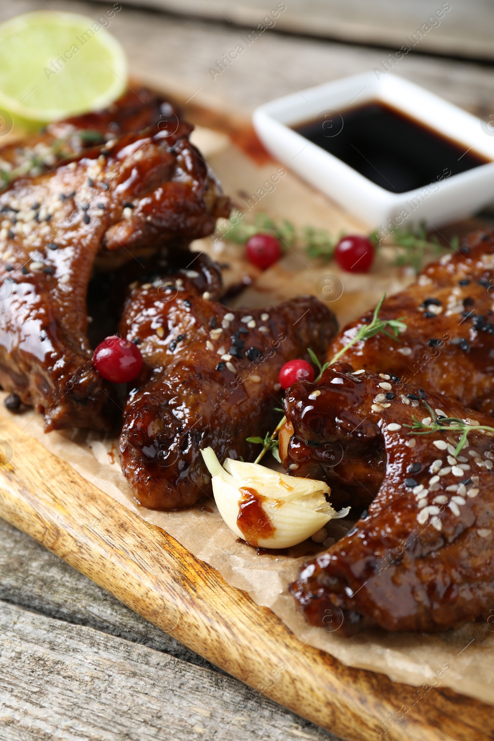 Photo of Tasty chicken wings glazed in soy sauce with garnish on wooden table, closeup