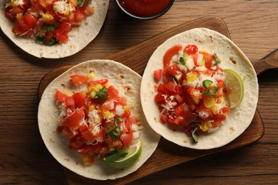 Photo of Delicious tacos with vegetables, lime and ketchup on wooden table, flat lay