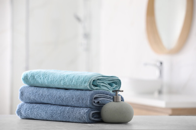 Photo of Stack of fresh towels and soap dispenser on table in bathroom