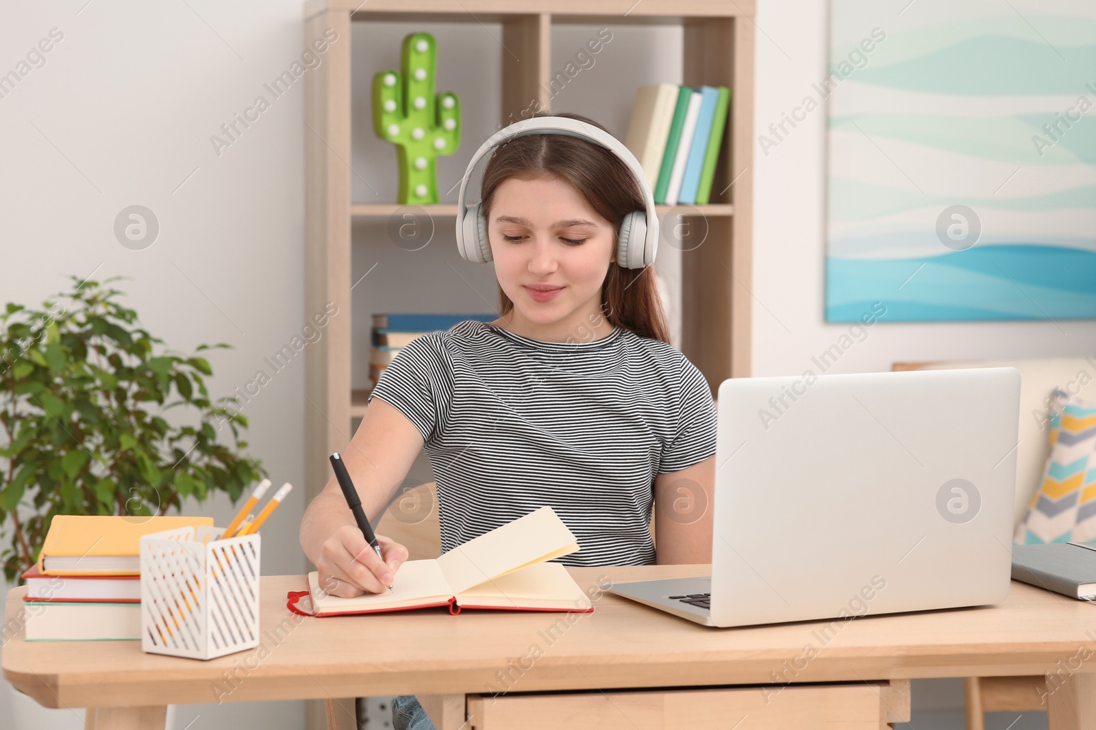 Photo of Cute girl using laptop and headphones at desk in room. Home workplace