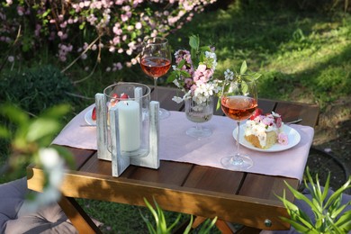 Vase with spring flowers, wine and cake on table served for romantic date in garden