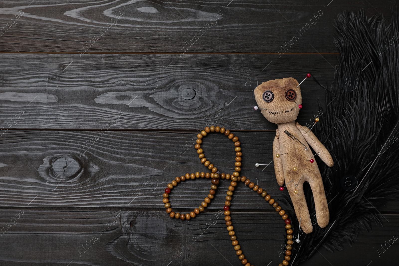 Photo of Voodoo doll pierced with pins, beads and feather on black wooden table, flat lay. Space for text