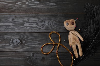Voodoo doll pierced with pins, beads and feather on black wooden table, flat lay. Space for text