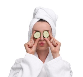 Photo of Beautiful woman in bathrobe covering eyes with pieces of cucumber and blowing kiss on white background