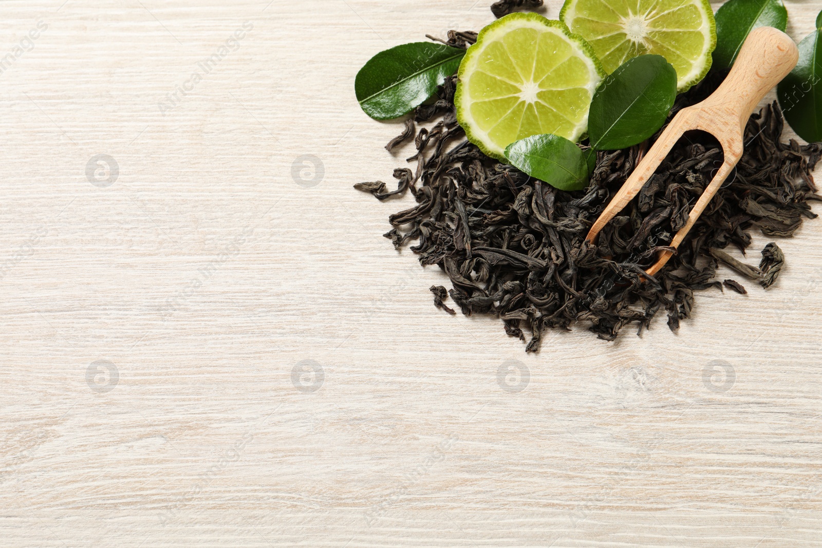 Photo of Pile of dry bergamot tea leaves and fresh fruit on light wooden table, flat lay. Space for text