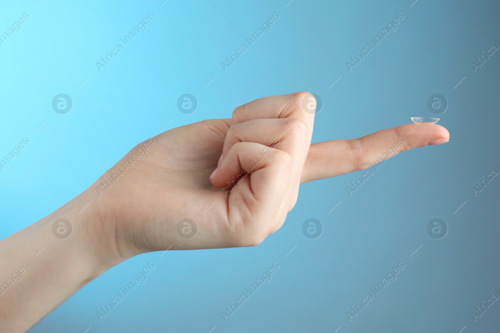 Photo of Woman holding contact lens on light blue background, closeup