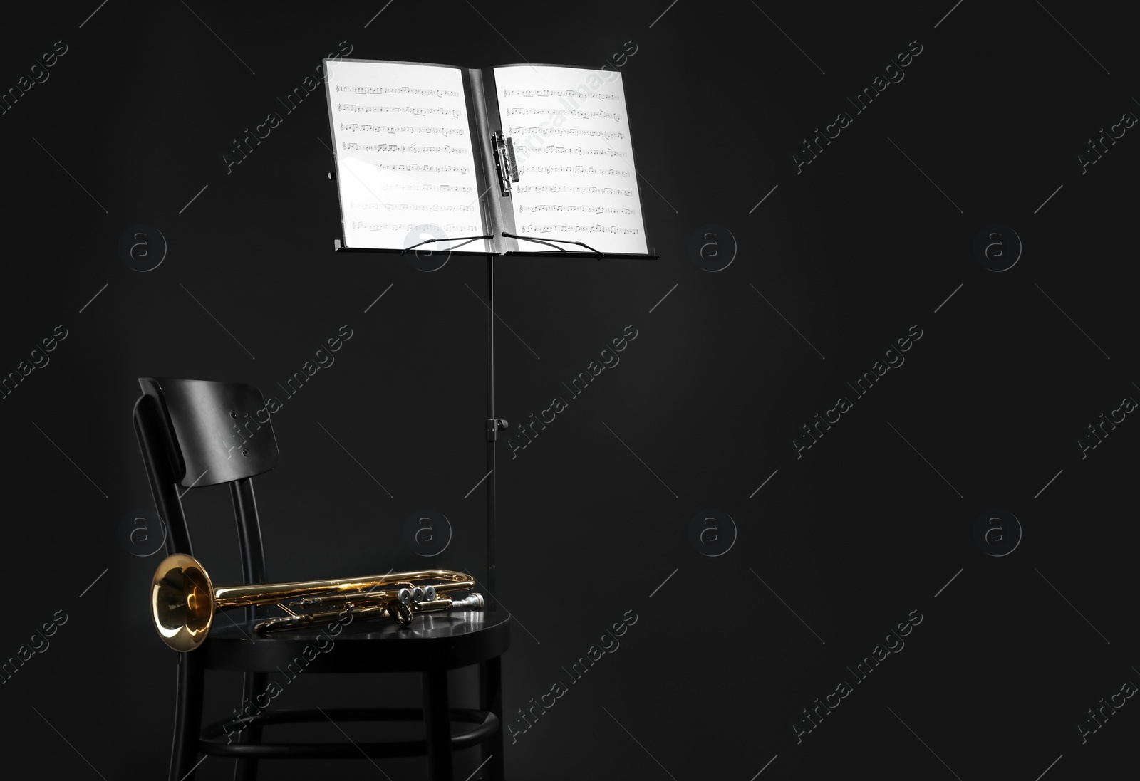 Photo of Trumpet, chair and note stand with music sheets on black background. Space for text