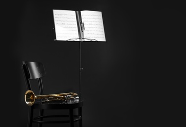 Trumpet, chair and note stand with music sheets on black background. Space for text