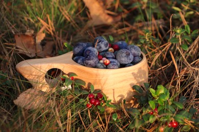 Photo of Wooden mug full of fresh ripe blueberries and lingonberries on grass