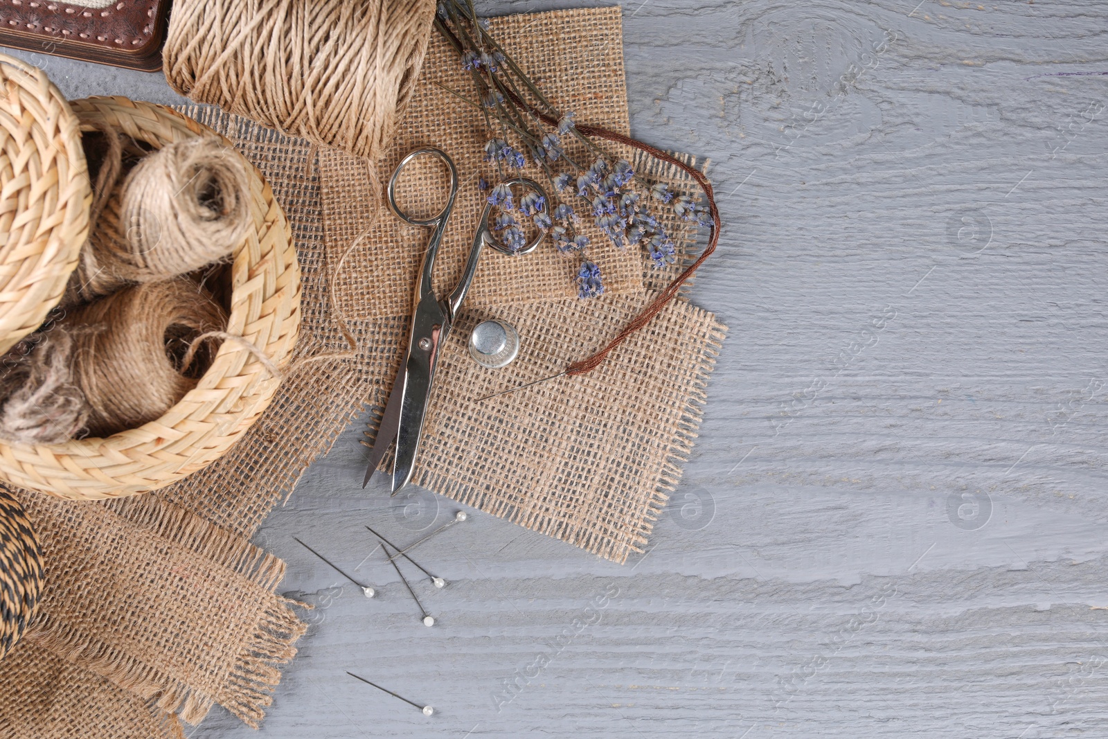 Photo of Pieces of burlap fabric and sewing tools on grey wooden table, flat lay. Space for text