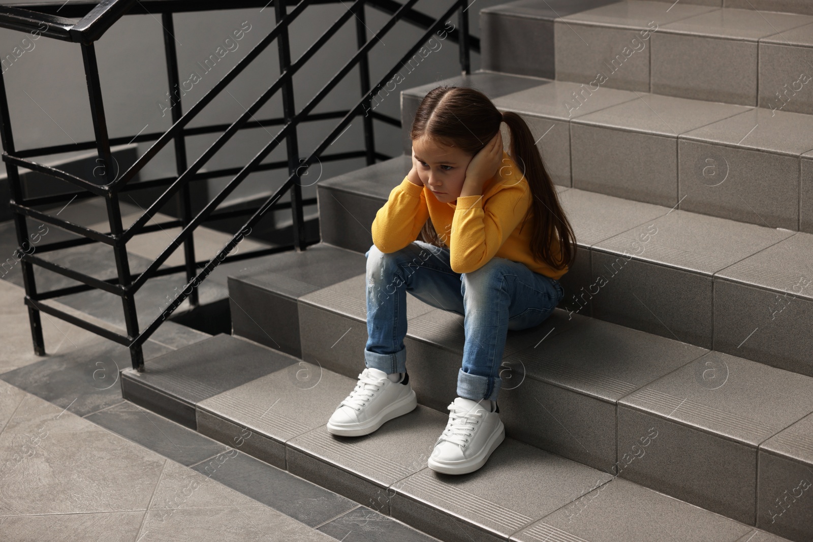 Photo of Child abuse. Upset little girl sitting on stairs indoors