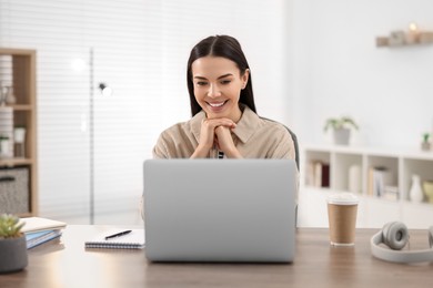 Young woman watching webinar at table in room