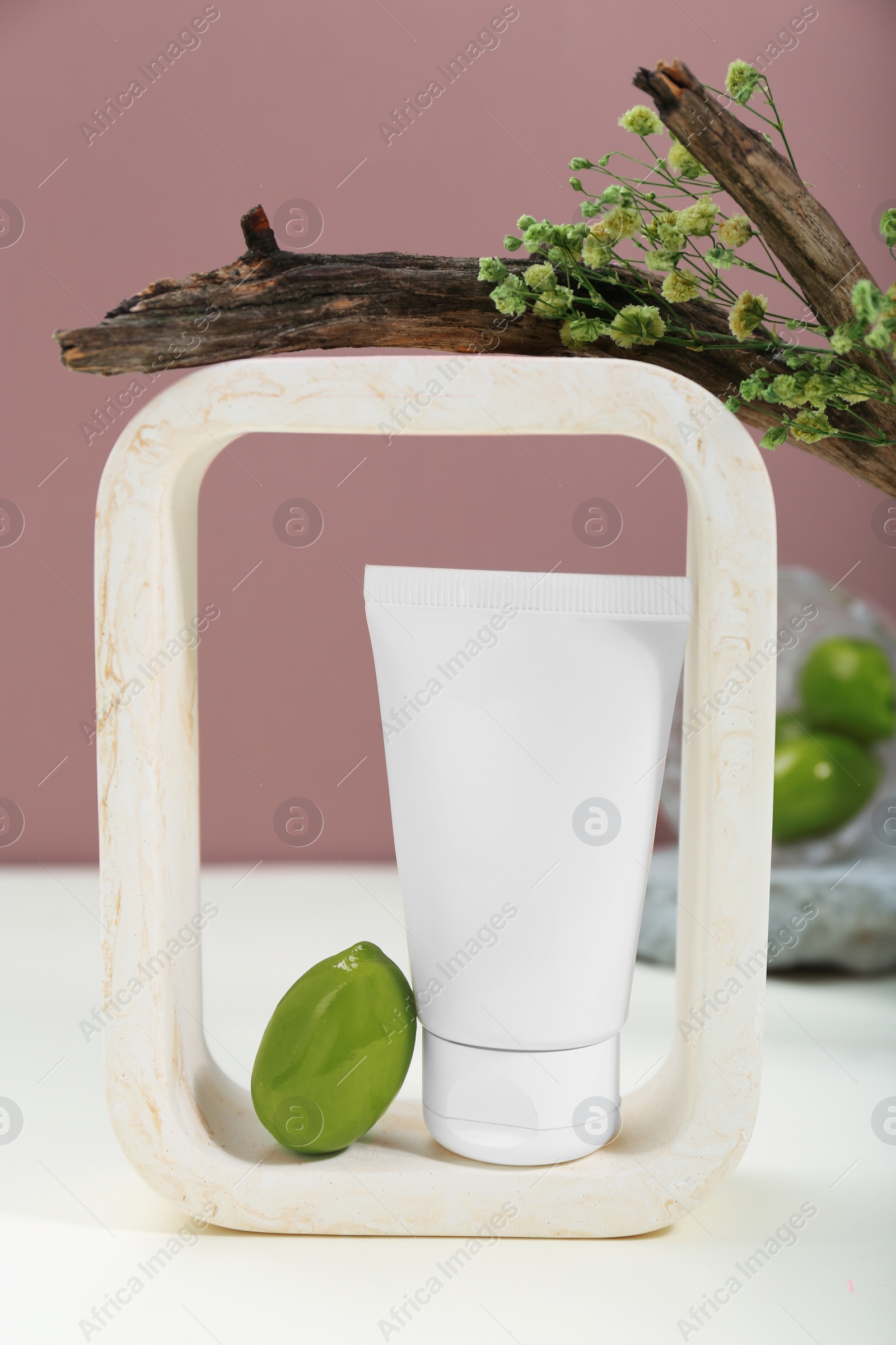 Photo of Tube of cream and olives on white table against pink background